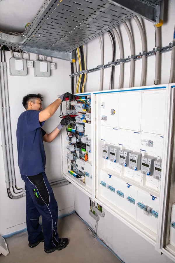 Elektroniker arbeitet an einer raumhohen Verteileranlage im Technikraum